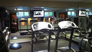 Une salle de sport équipée de tapis de course, d’appareils d’exercice et de plusieurs écrans diffusant des vidéos d’entraînement.