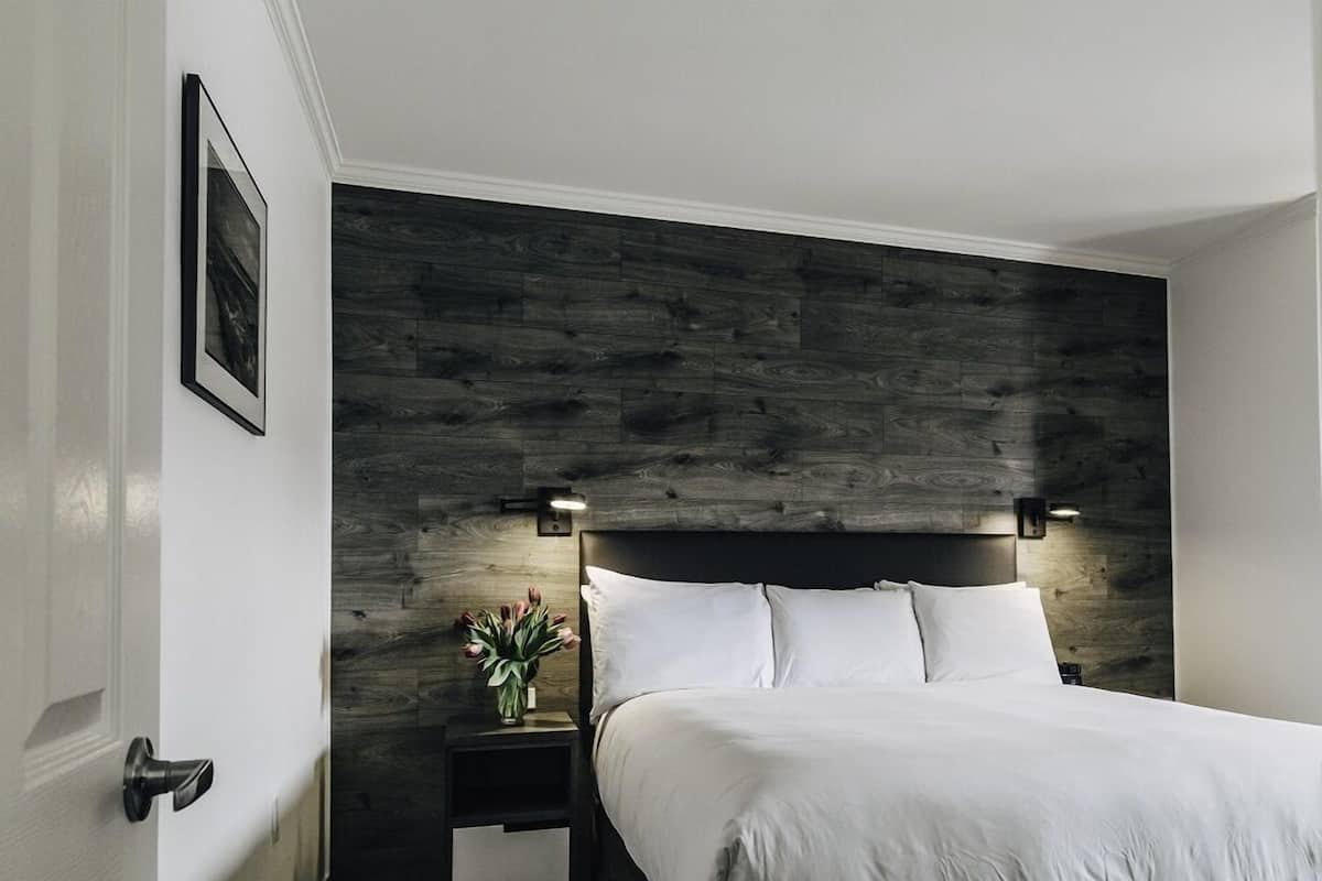 Quarto com cabeceira de madeira, mesa de cabeceira com um vaso de flores e um quadro na parede.