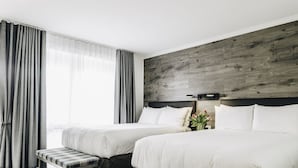 Une chambre d’hôtel avec deux lits, un banc, un mur décoratif en bois et une fenêtre avec des rideaux.