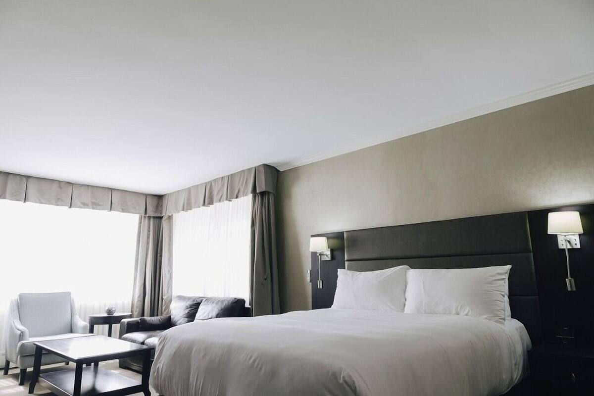 Quarto de hotel com uma cama grande, uma escrivaninha, uma cadeira e uma janela com cortinas.