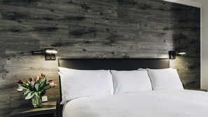 A bed with white bedding, a dark headboard, and two wall-mounted lights. - The Hotel on Pownal (Charlottetown)