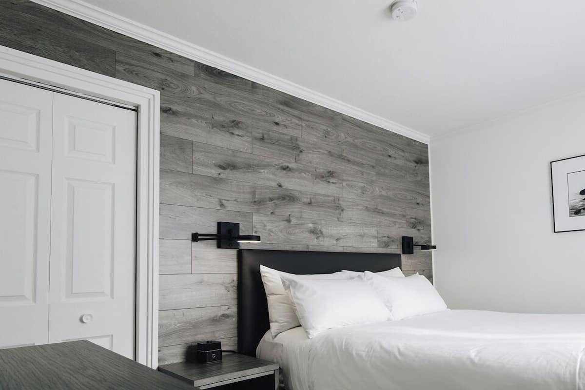 Quarto com cabeceira de madeira, porta branca, mesa de cabeceira com abajur e quadro na parede.