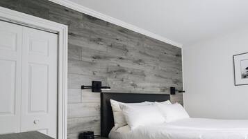 Un dormitorio con cabecera de madera, una puerta blanca, una mesita de noche con lámpara, y un cuadro enmarcado en la pared.