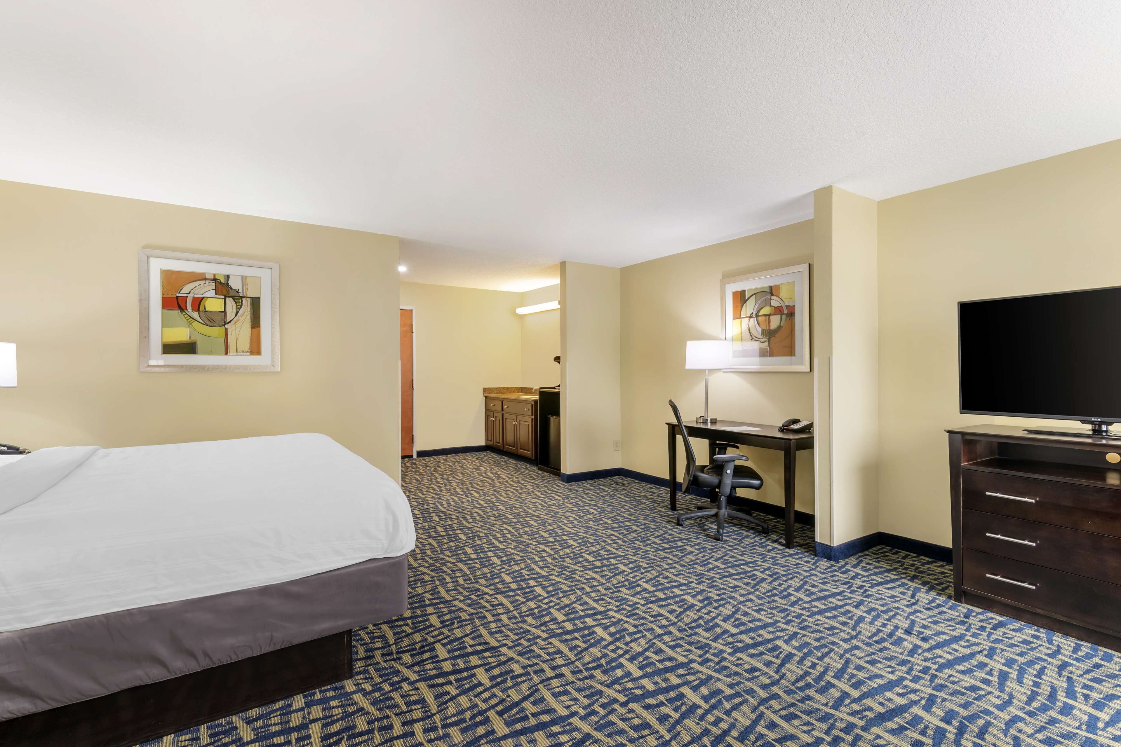 A hotel room with a bed, desk, chair, television, and artwork on the walls.