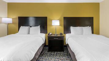 A hotel room with two beds, a nightstand with a lamp, and a phone.