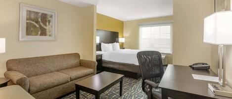 A hotel room with a bed, a sofa, a desk, a chair, a lamp, and a window.