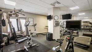 Una palestra con attrezzature per esercizi, tapis roulant, biciclette da spinning e una televisione appesa al muro.