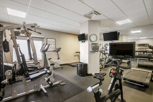 Un gimnasio con equipo de ejercicio, una caminadora, bicicletas estáticas y una televisión en la pared.
