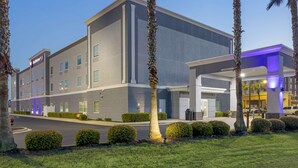 Un hotel moderno con più piani, dotato di un prato curato, palme e cielo sereno.