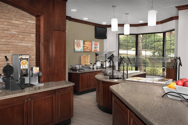 A kitchen with granite countertops, wooden cabinets, a coffee station, and a large window with a view of trees.