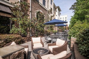 An outdoor patio area with wicker furniture, a round table with a fire pit, and a blue umbrella. - Staybridge Suites North Charleston by IHG (North Charleston)
