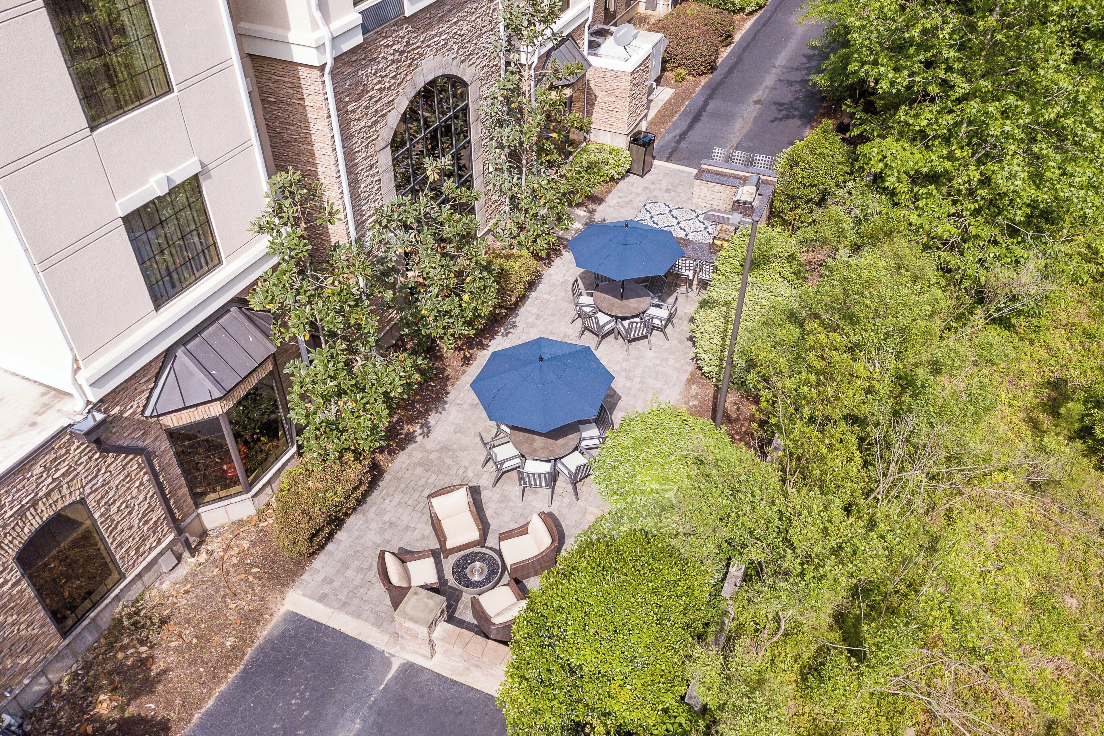 An outdoor patio area with tables and umbrellas, surrounded by trees and a building.