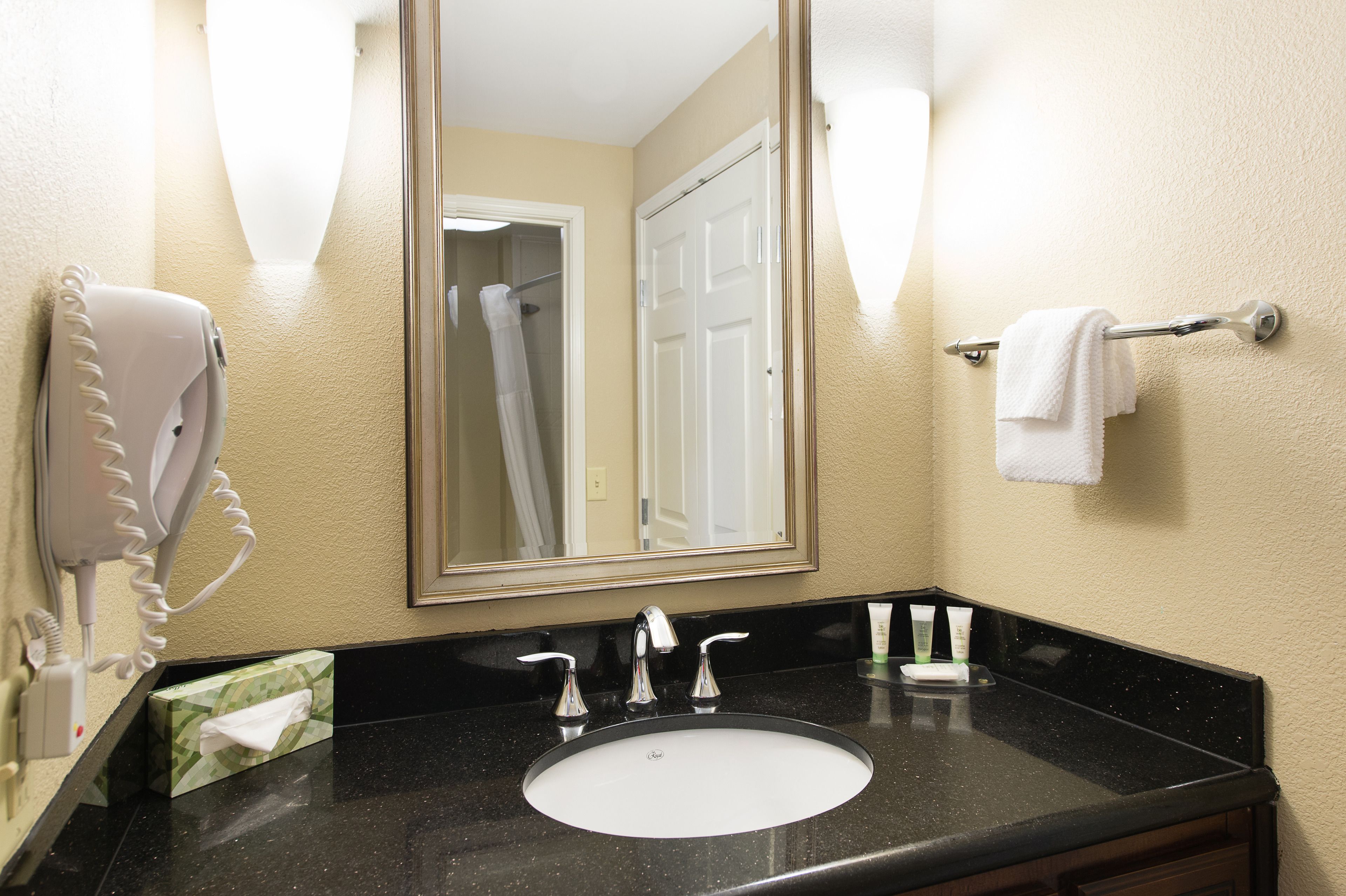 A hotel bathroom with a sink, mirror, towel rack, and hairdryer.