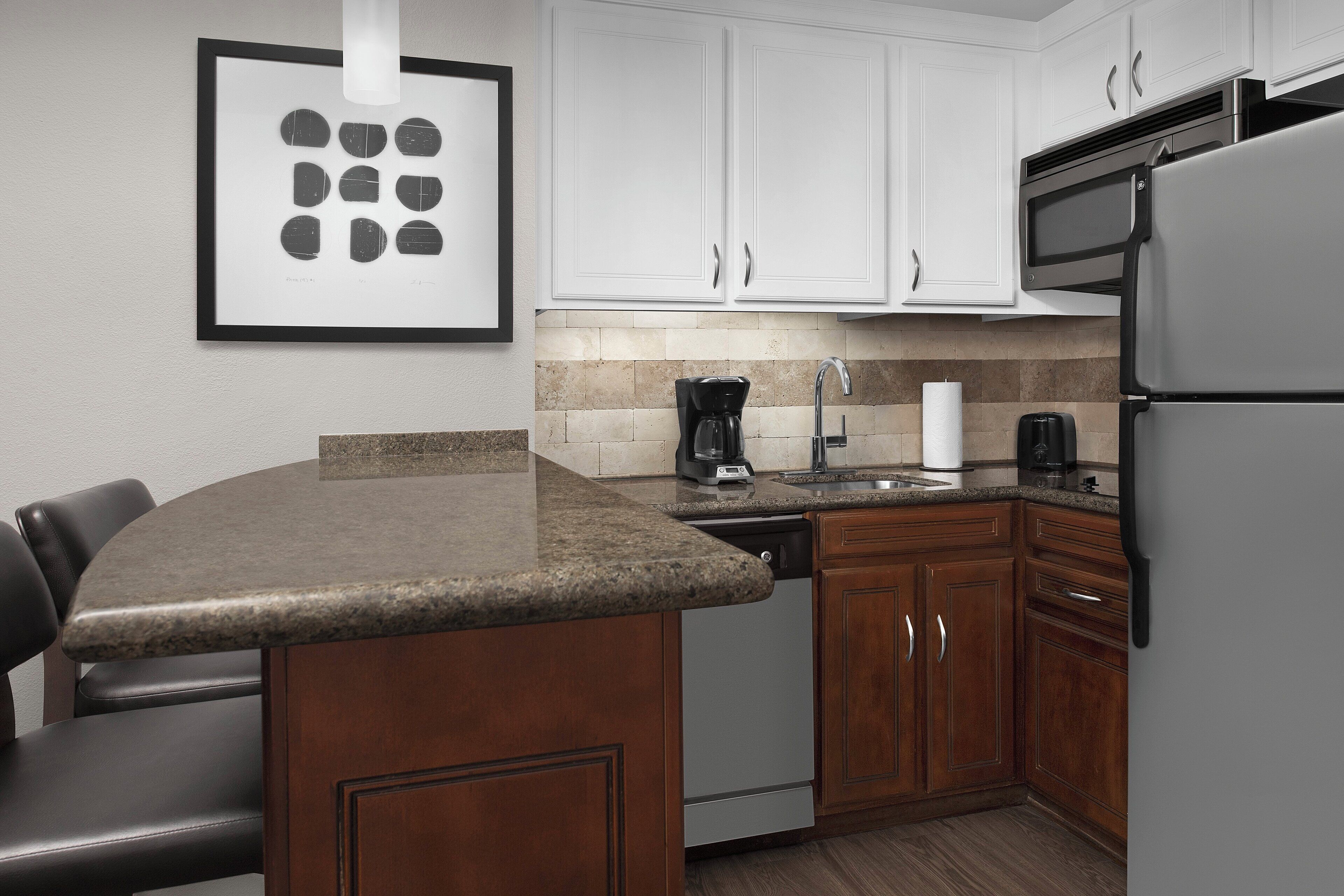 A kitchen with white cabinets, a granite countertop, a built-in dishwasher, a stainless steel refrigerator, and a microwave.