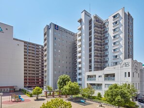 Un hotel de varios pisos con un diseño moderno, con balcones, una terraza en la azotea y un área de juegos.