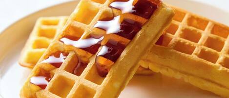 Two waffles with syrup being poured over them.
