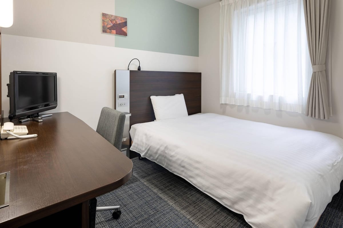 Ein Hotelzimmer mit Bett, Schreibtisch mit Telefon, Fernseher und Bedienfeld an der Wand.