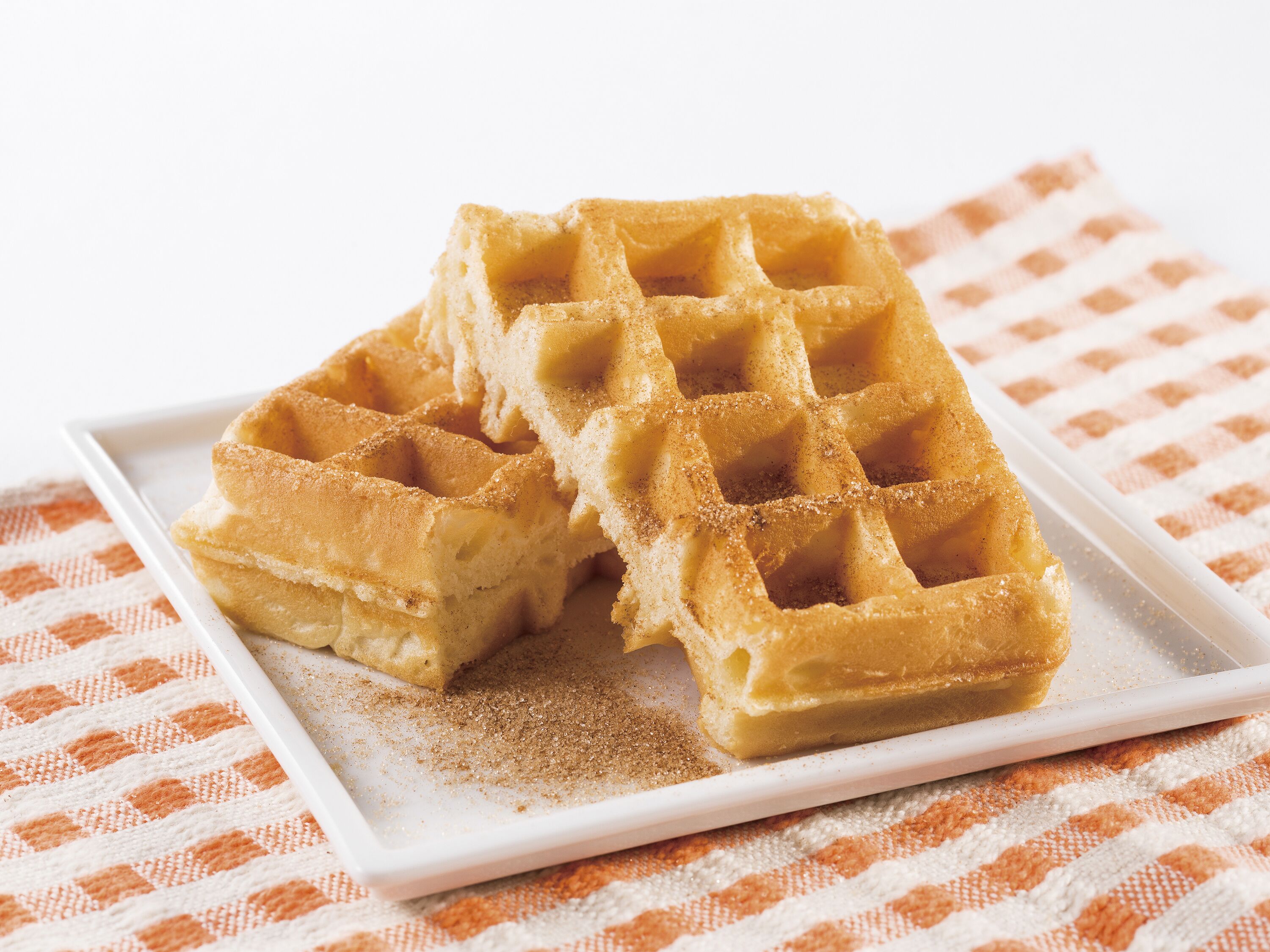 Ein Stapel Waffeln auf einem weißen Teller, darunter eine karierte Tischdecke.
