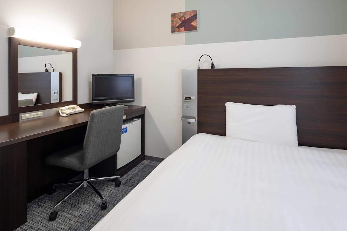 Una habitación de hotel con una cama, un escritorio con computadora, una silla, un teléfono, dispensador de agua y un espejo.