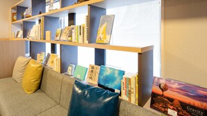 A library with bookshelves, a sofa with cushions, and a poster. - Comfort Hotel Kure (Kure)