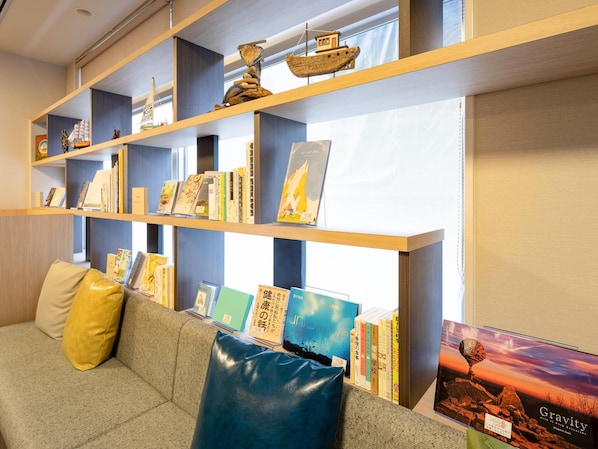 Una biblioteca con estanterías, un sofá con cojines y un cartel.