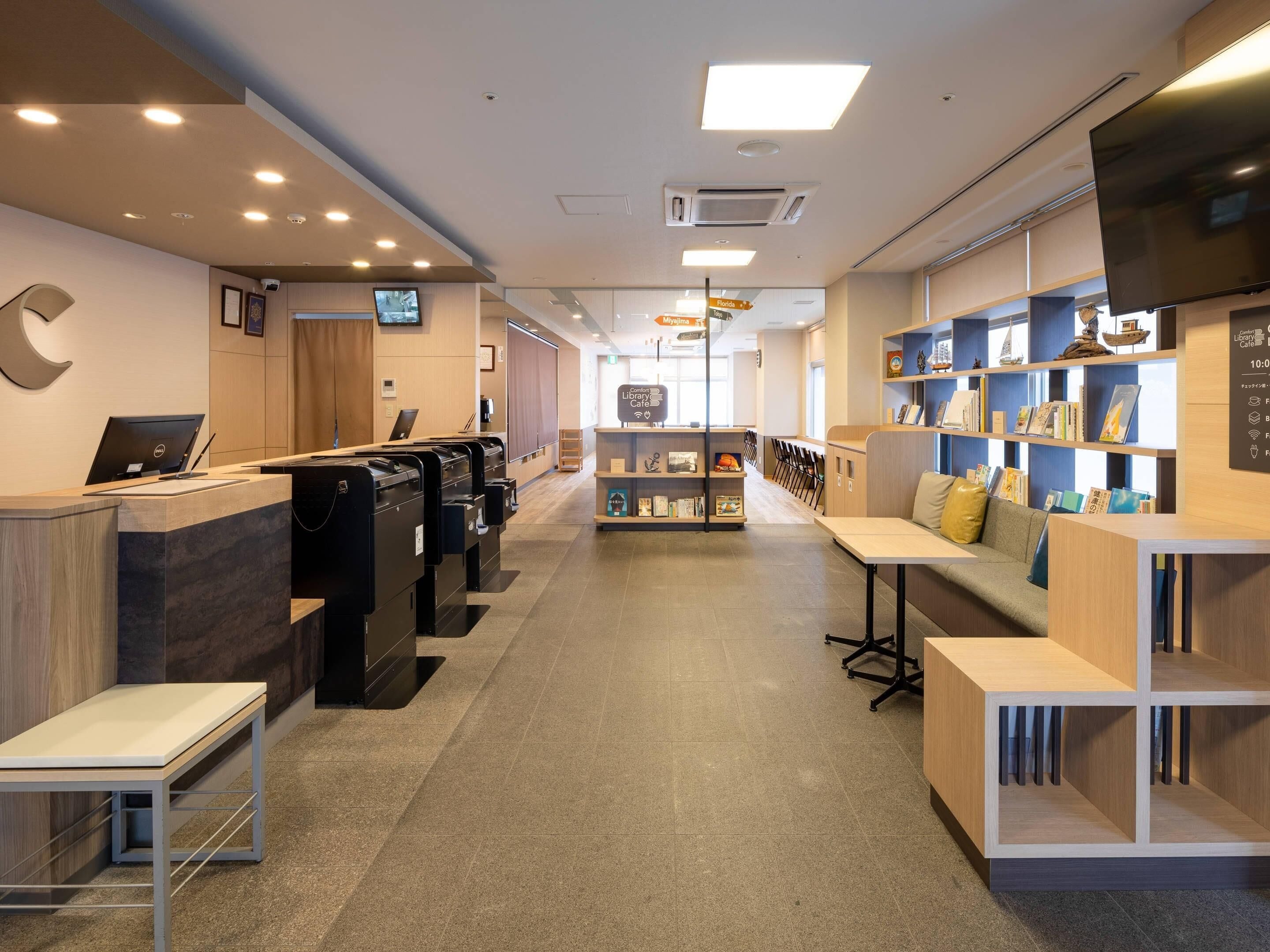 Un moderno vestíbulo de hotel con mostrador de recepción, zona de estar y una estantería con libros y objetos decorativos.