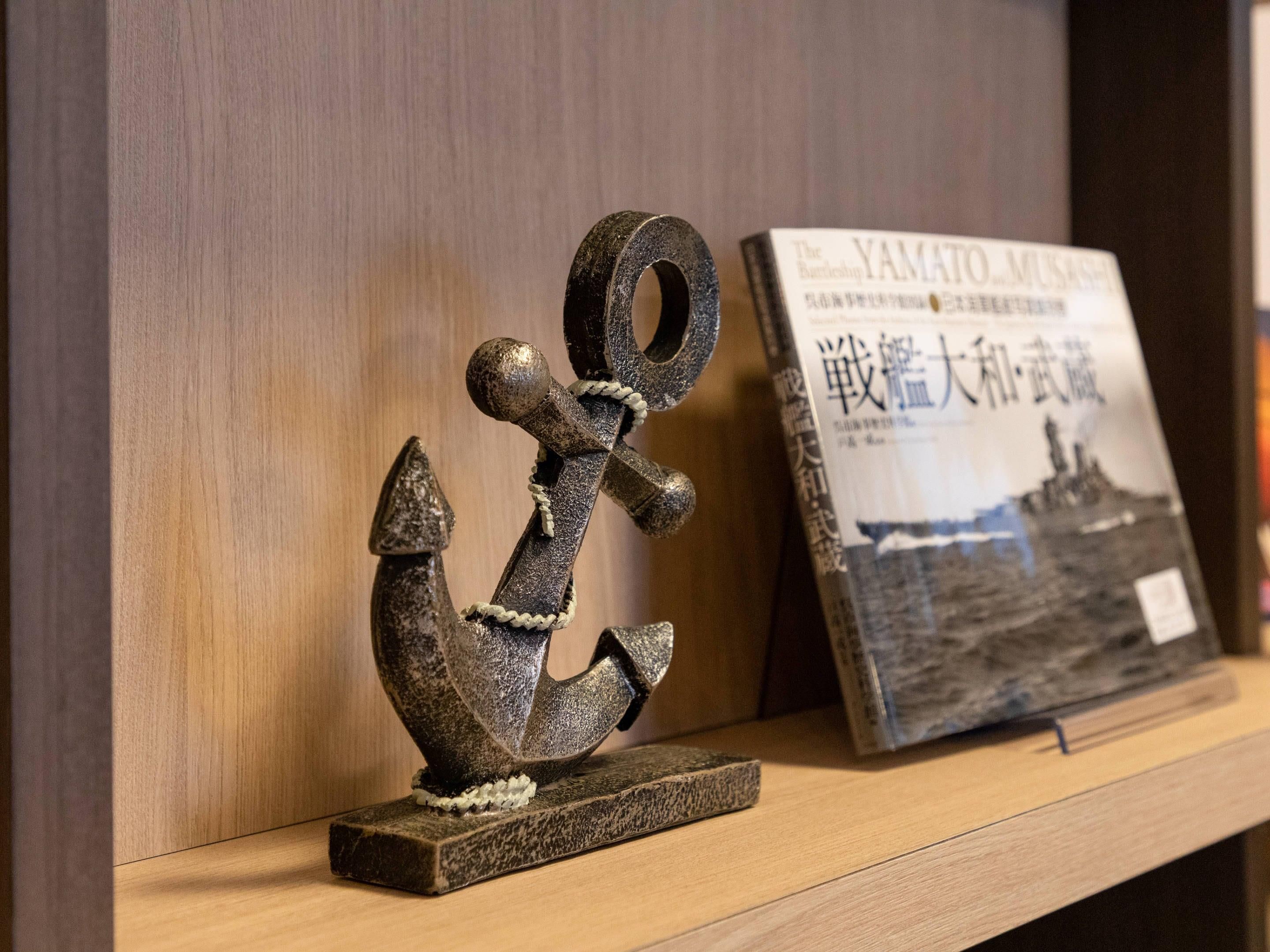 A wooden shelf with a metal anchor sculpture and a book titled 'The Battle of YAMATO MUSASHI'.
