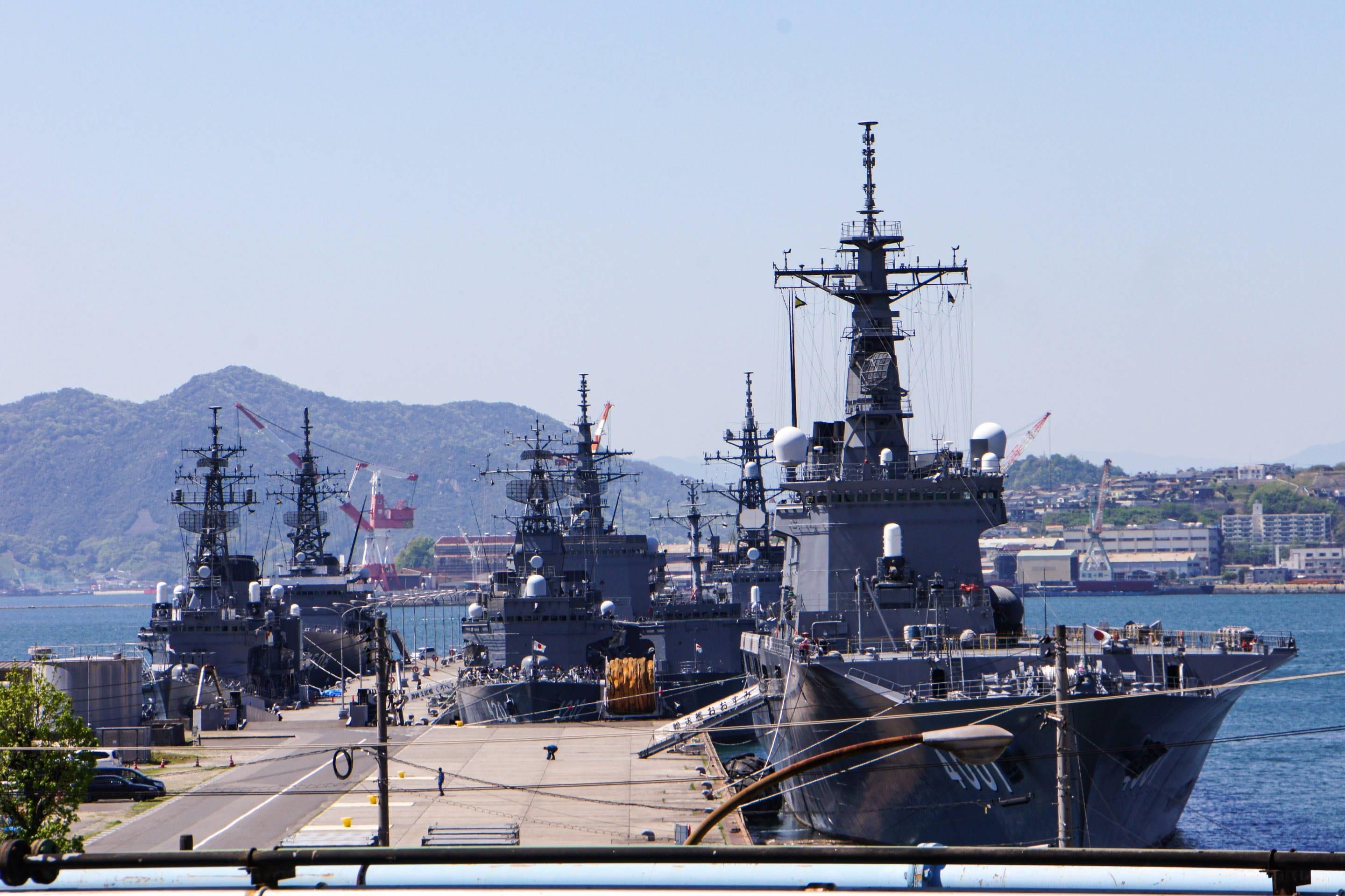 A naval ship docked at a port with a mountainous backdrop.