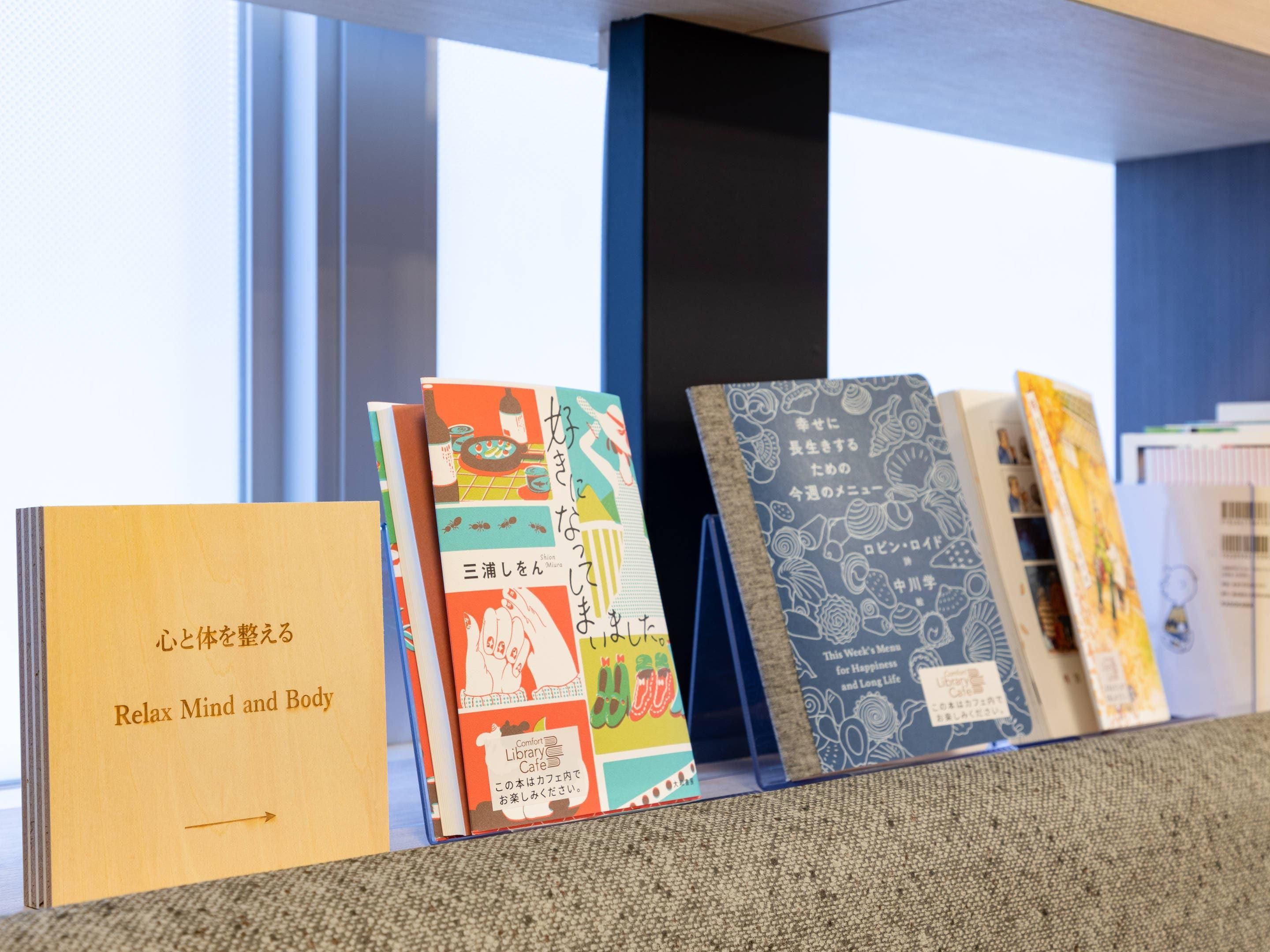 A row of books on a shelf with Japanese text, a wooden book titled 'Relax Mind and Body', and a blue book with a pattern.