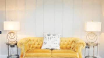 A yellow sofa with a tufted design, a glass coffee table, and two lamps on side tables.