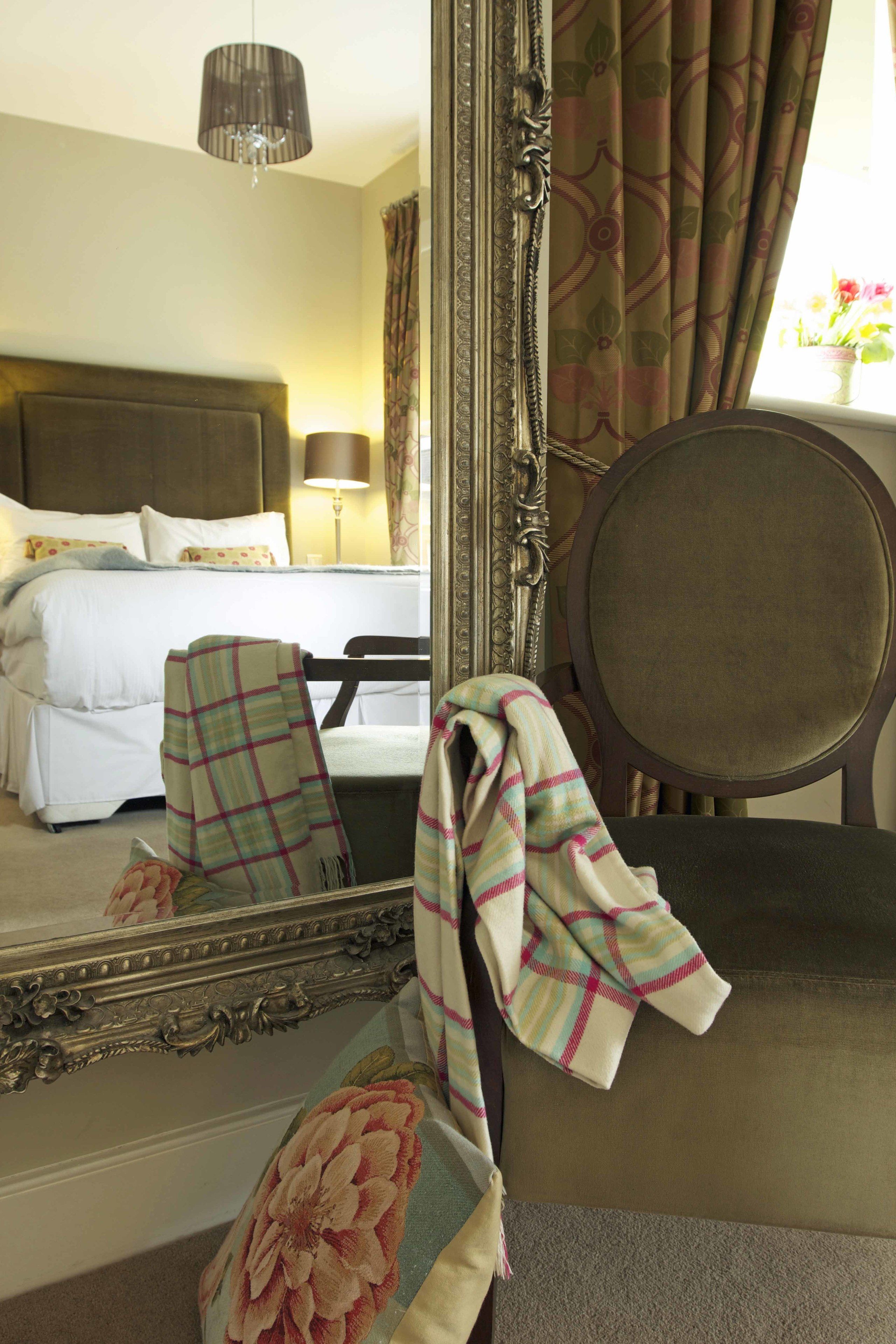 A hotel room with a bed, a chair, a mirror, and a window with curtains.