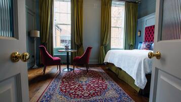 Une chambre avec un grand lit, un fauteuil rouge, une petite table et un tapis à motifs.