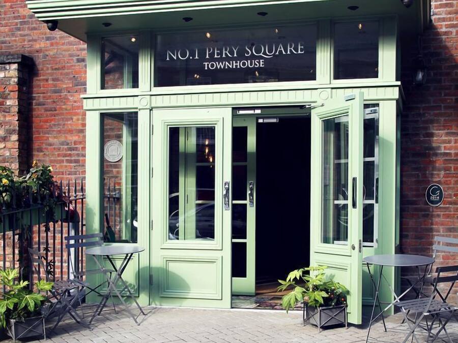 L'esterno della townhouse al numero 1 di Perry Square, con facciata verde, ampie finestre e un piccolo spazio esterno arredato con tavoli e sedie.
