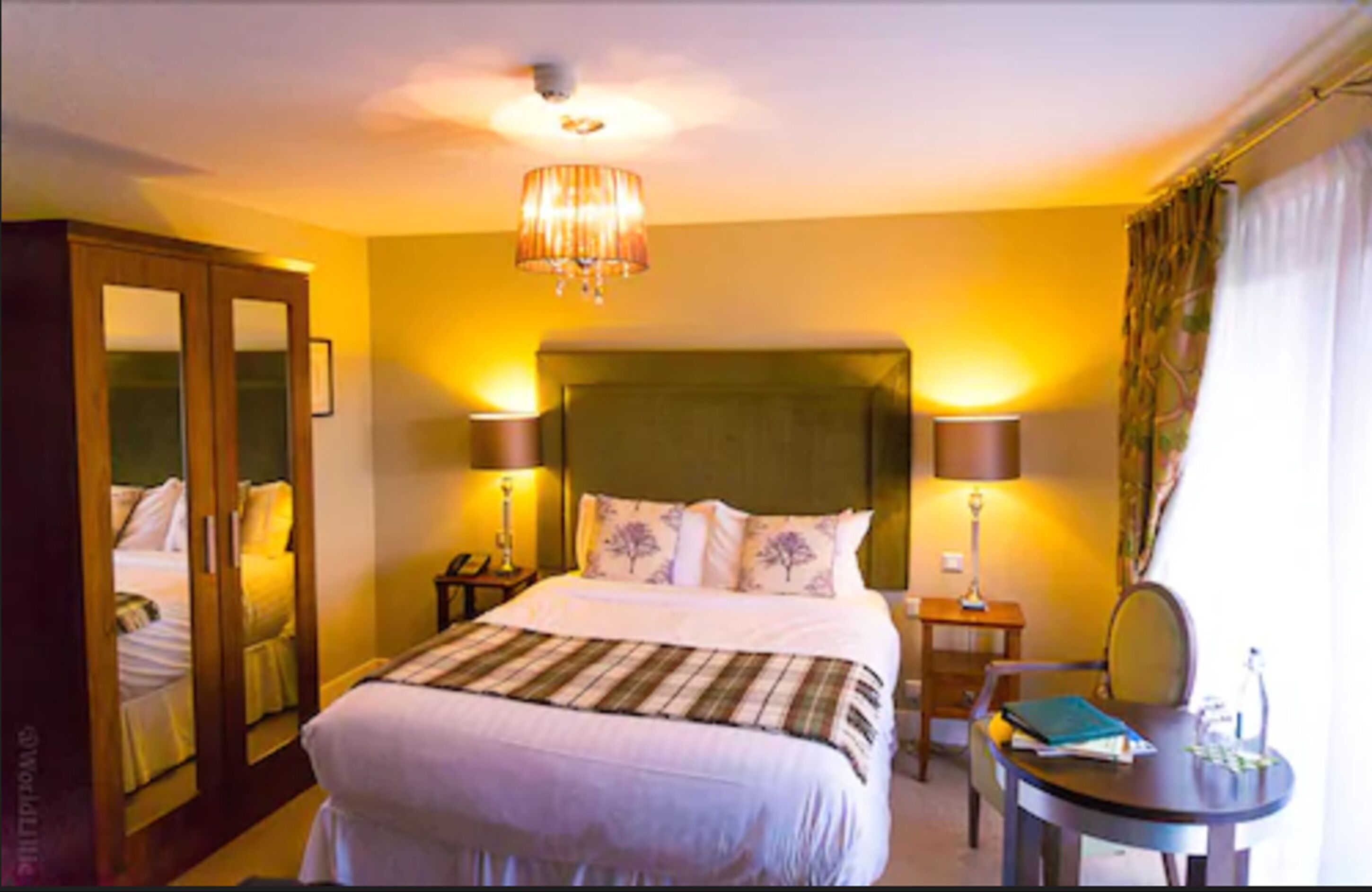 Een hotelkamer met een groot bed, twee bedlampen, een spiegel, een klein tafeltje en een stoel.