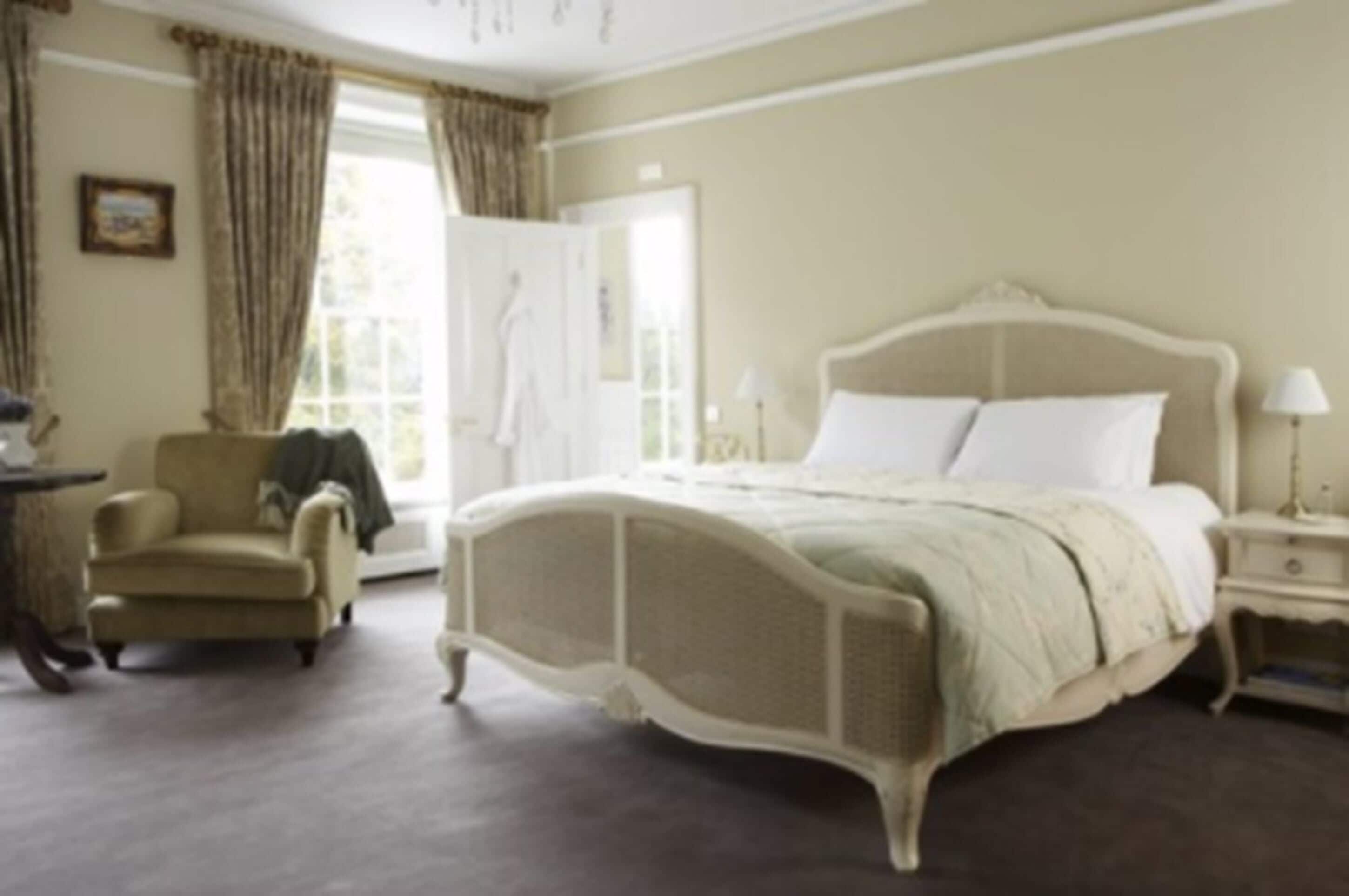 A bedroom with a large bed, a chair, a nightstand, and a window with curtains.