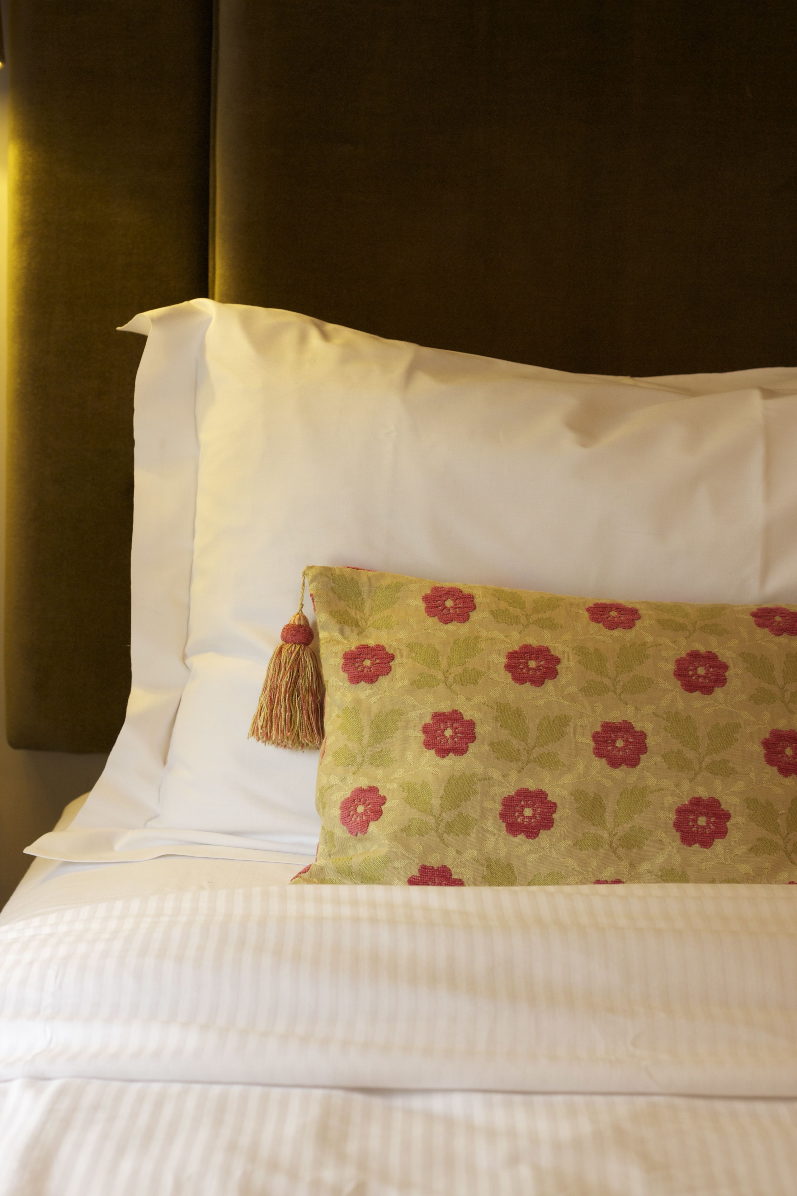 Ein ordentlich bezogenes Bett mit weißen Leinen und einem einzelnen, dekorativen Kissen mit Blumenmuster.