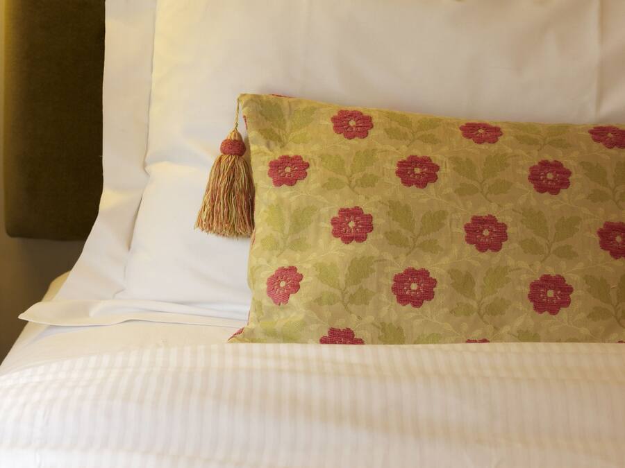 A neatly made bed with white linens and a single decorative pillow with a floral pattern.