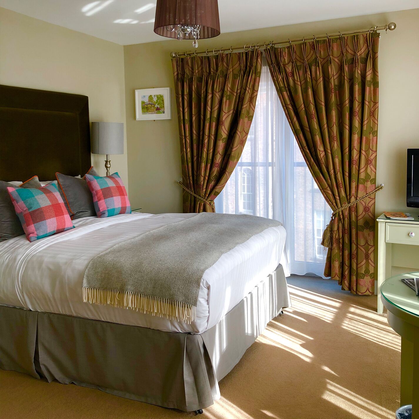 A hotel room with a large bed, a bedside table, a lamp, a TV, and a window with curtains.