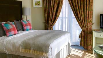 A hotel room with a large bed, a bedside table, a lamp, a TV, and a window with curtains.
