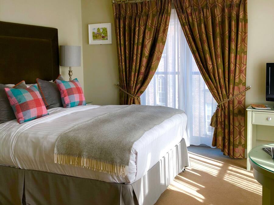 A hotel room with a large bed, a bedside table, a lamp, a TV, and a window with curtains.