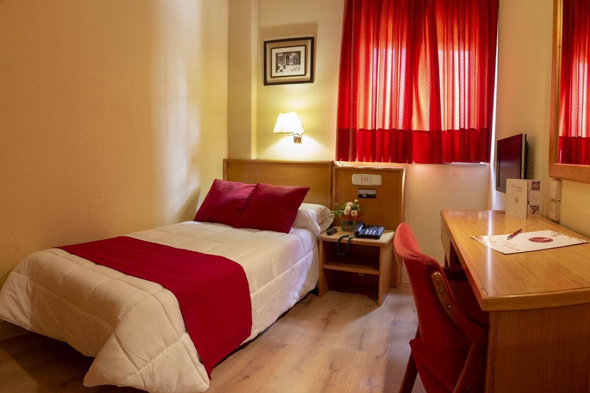 Une chambre d’hôtel équipée d’un lit, d’un bureau, d’une chaise, d’une lampe, d’un téléphone et d’un téléviseur.