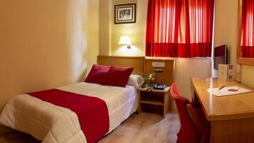 A hotel room with a bed, a desk, a chair, a lamp, a telephone, and a television.
