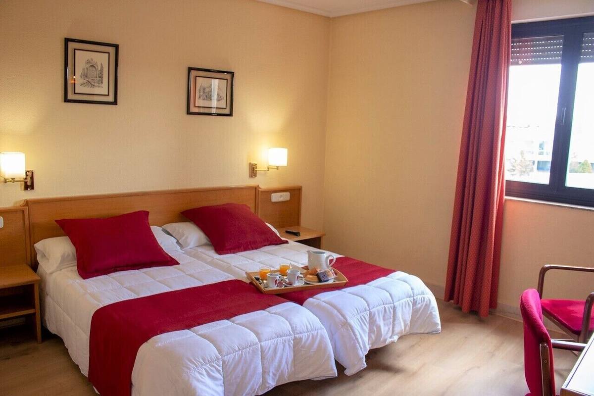 Une chambre d’hôtel avec deux lits, des oreillers rouges, un plateau avec des articles pour le petit-déjeuner et des tableaux encadrés accrochés au mur.