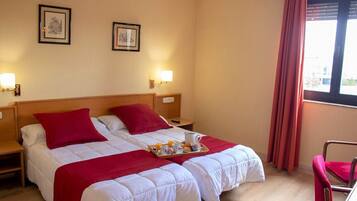 Une chambre d’hôtel avec deux lits, des oreillers rouges, un plateau avec des articles pour le petit-déjeuner et des tableaux encadrés accrochés au mur.