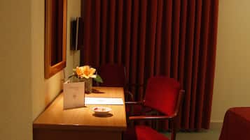 Una habitación de hotel con un escritorio de madera, una silla roja, una cama con cubierta roja, un espejo y un televisor montado en la pared.
