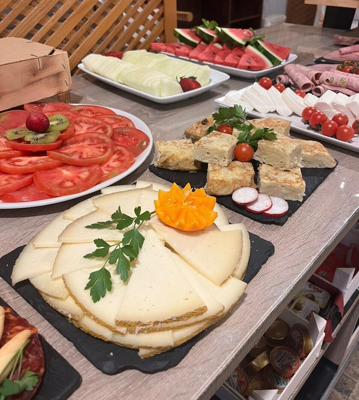 A buffet table with various food items including sliced tomatoes, watermelon, cheese, and other dishes.