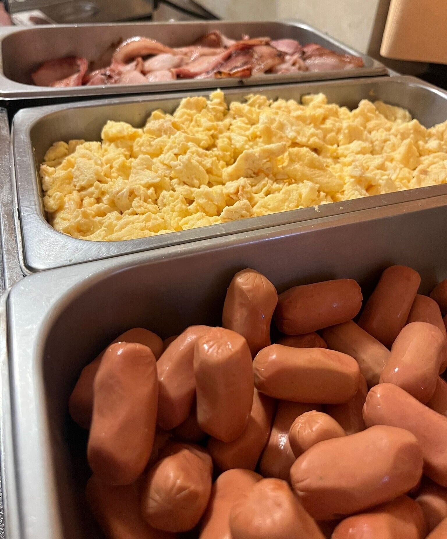 A buffet with scrambled eggs, bacon, and sausages.