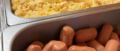 Un bufé con huevos revueltos, tocino y salchichas.