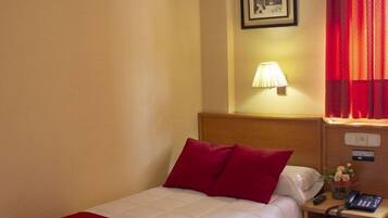 A hotel room with a bed, a nightstand, a lamp, and a red curtain.