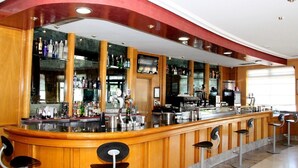 Una zona de bar con una barra de madera curva, varios taburetes y estantes llenos de botellas.
